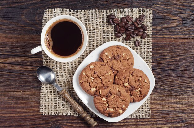 Kaffee mit Schokoladenkeksen auf dunklem Holztisch von oben
