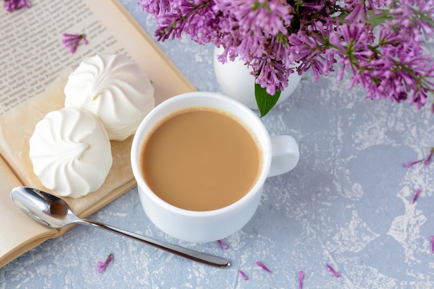 Kaffee oder Tee mit Milch und Marshmallows. Ein Buch im Garten mit einer Tasse Kaffee lesen. Romantisches Stillleben mit lila Blumen.