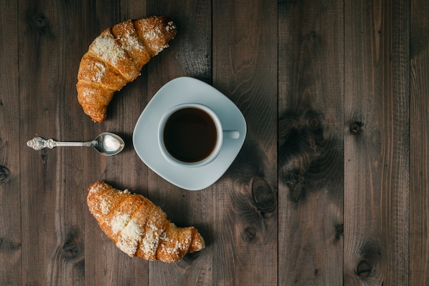 Kaffee und Croissant zum Frühstück auf rustikalem Holztisch, Draufsicht