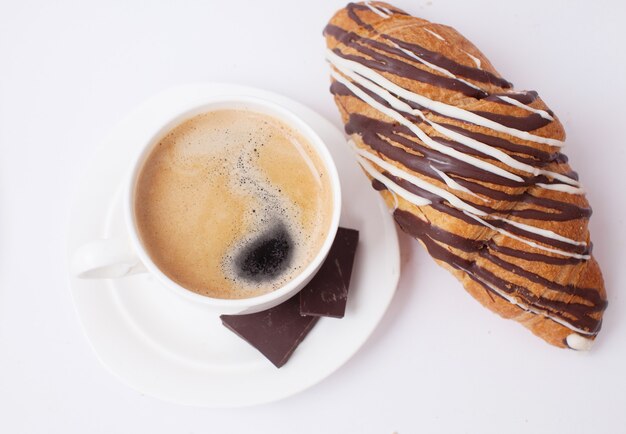 Kaffee und Croissant zum Frühstück auf weißem Tisch