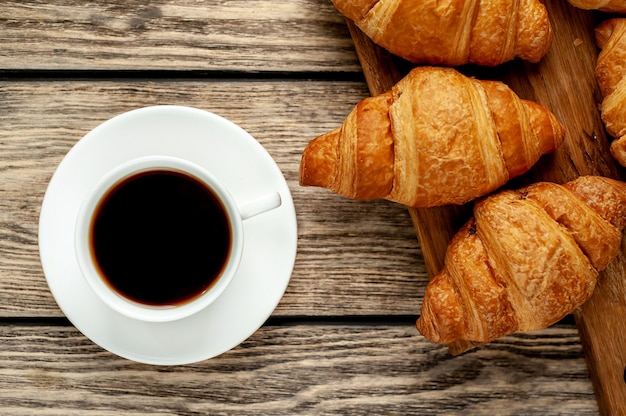 Kaffee und Croissants auf einem hölzernen Schneidebrett, auf Holzhintergrund