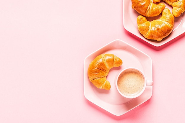 Kaffee und Croissants zum Frühstück auf einem rosa Hintergrund, Draufsicht, flache Lage.