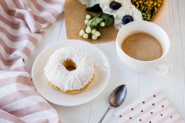 Kaffee und ein Donut mit frischen Blumen