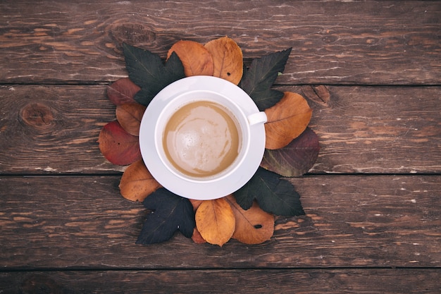 Kaffee und Herbstlaub auf Holzuntergrund