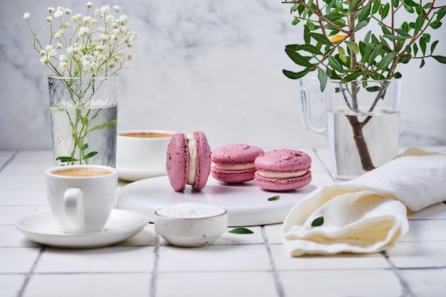 Kaffee und Macarons Kuchen zum Frühstück für zwei Morgentisch mit Dessert Espresso und Blumen in einer Vase auf einem weiß gefliesten Tisch