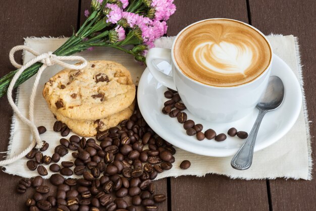 Kaffee und purpurrote blume witn bohne und weißes glas, teller, stoff auf braunem hölzernem