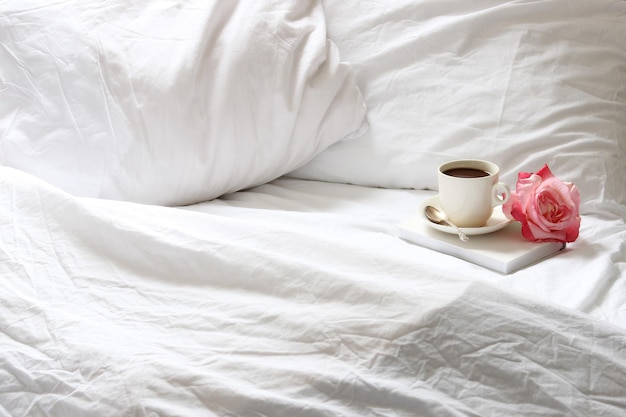 Kaffeebecher und Rose im Bett zu Hause