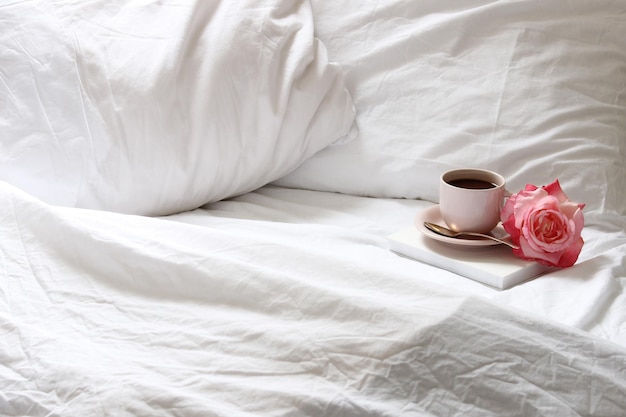 Kaffeebecher und Rose im Bett zu Hause