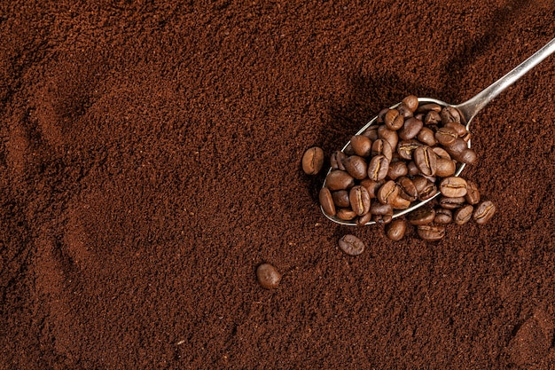 Kaffeebohnen auf Löffel auf gemahlenem Kaffeehintergrund. Nahansicht.