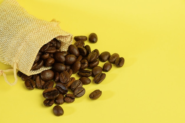 Kaffeebohnen aus einem kleinen Beutel auf gelbem Grund auf der linken Seite verstreut.
