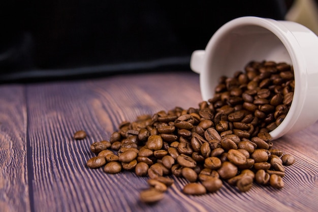 Kaffeebohnen aus einer weißen Tasse auf einem Holztisch