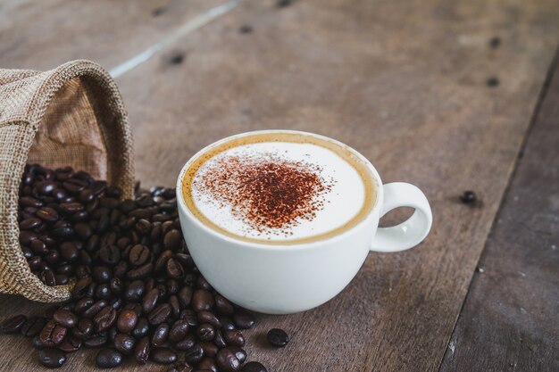 Kaffeebohnen im Sack mit einer Kaffeetasse auf Holztischhintergrund.