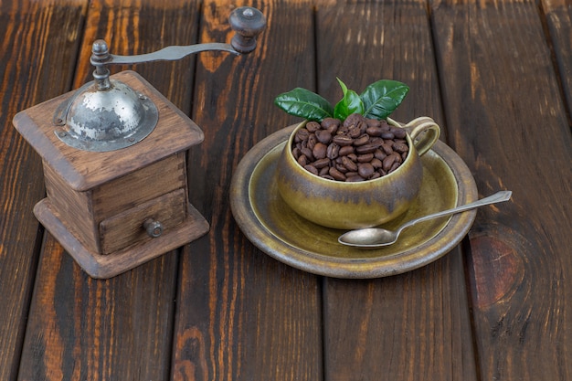 Kaffeebohnen in einer Tasse und alte manuelle Kaffeemühle auf einem Holztisch