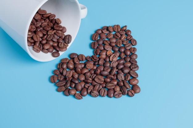 Kaffeebohnen in einer weißen Tasse Kaffeebohnen sind in Form eines Herzens auf einem Türkis verstreut