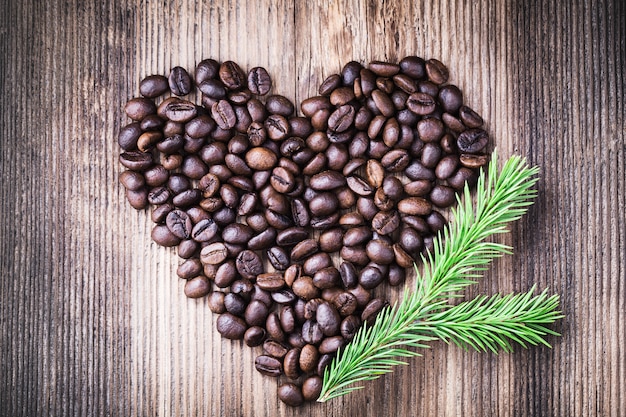 Kaffeebohnen in Form des Herzens mit Tannenbaumast auf Holzoberfläche