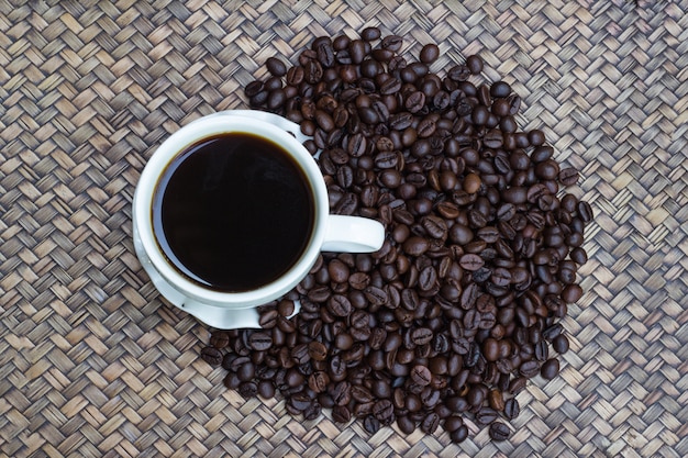 Foto kaffeebohnen mit weißem kaffeebecherunschärfehintergrund, eine tasse heißen kaffee wird neben die kaffeebohnen gesetzt