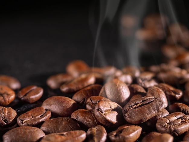Kaffeebohnen schließen auf einem schwarzen glänzenden Hintergrund.