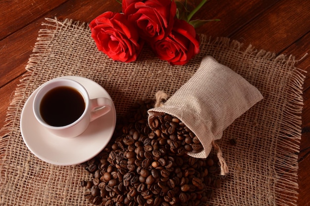 Kaffeebohnen und eine Tasse Kaffee und Rosenblüten