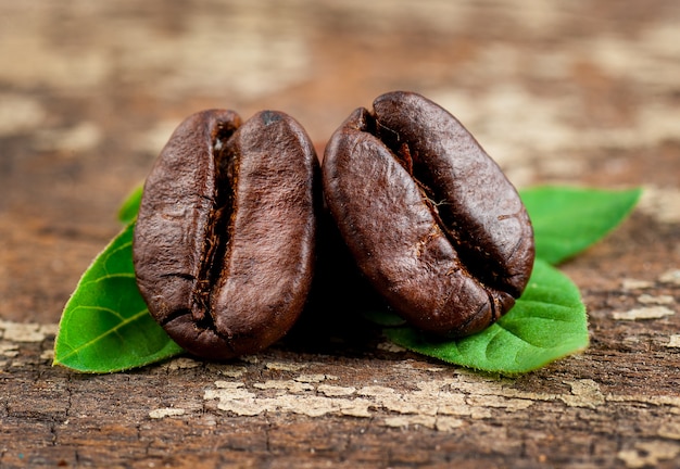 Kaffeebohnen und grünes Blatt auf hölzernem Hintergrund des Schmutzes