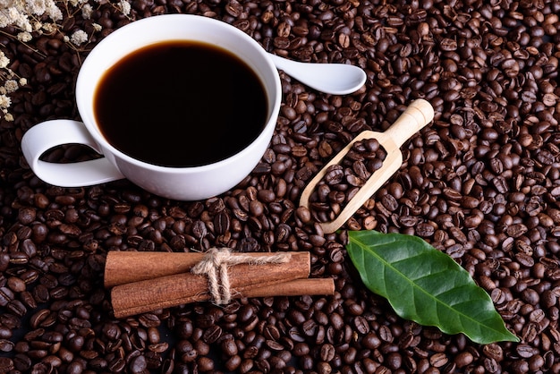 Kaffeebohnen und Kaffeeblatt mit Löffel auf schwarzem Holztisch