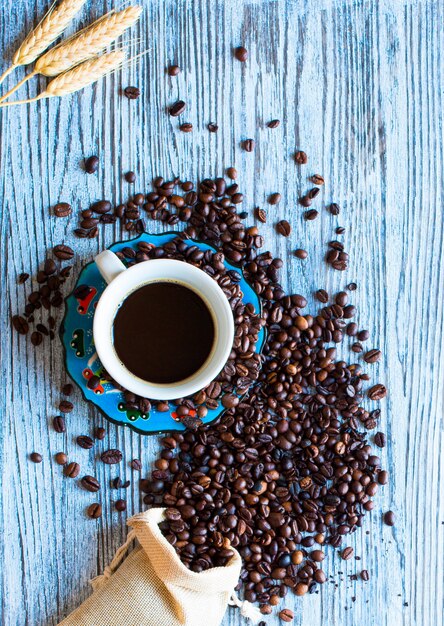 Kaffeebohnen und Tasse Kaffee mit anderen Komponenten auf unterschiedlicher Holzoberfläche.