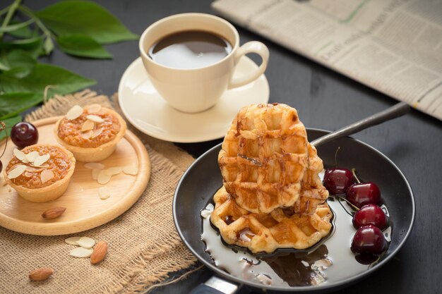 Kaffeegetränk Frühstückskonzept beinhaltet knusprige Torten mit Mandeln, Waffeln und frischen Kirschen