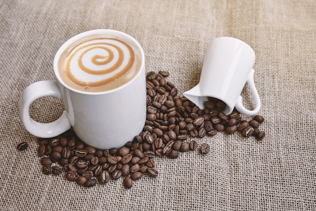 Kaffeekaramel macchiato mit Milchkunst und Kaffeebohnen auf Sackleinen