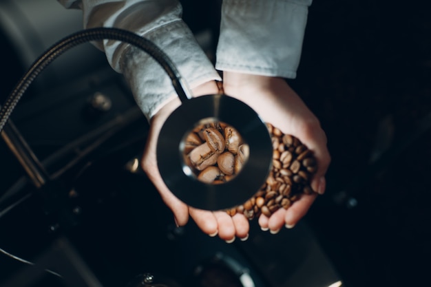 Kaffeekühlung in der Röstermaschine beim Kaffeeröstprozess junge Arbeiterin Barista mischen und halten Kaffeebohnen in den Händen an der Lupe