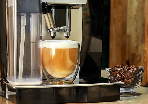 Kaffeemaschine macht Cappuccino-Kaffee in einer transparenten Tasse.