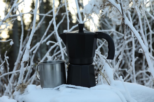 Kaffeemaschine und Metallbecher auf Baumstumpf im Wintertag