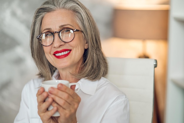 Kaffeepause. Elegante reife Frau, die Kaffee trinkt und friedlich aussieht