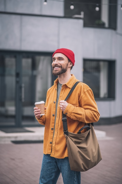 Kaffeepause. Mann in einem roten Hut und in einer orangefarbenen Jacke mit einer Kaffeetasse in den Händen