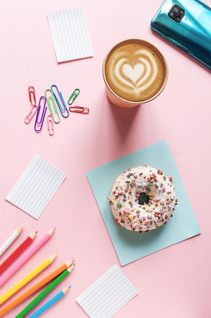 Kaffeepause mit Donut auf dem rosa Tischhintergrund