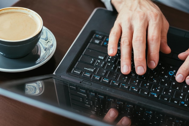 Kaffeepause und Arbeiterhände tippen auf Laptoptasse Latte auf dem Tisch