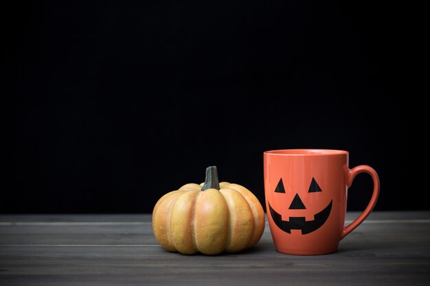 Kaffeetasse als Kürbislaterne Kürbis auf Holztisch. Halloween-Konzept