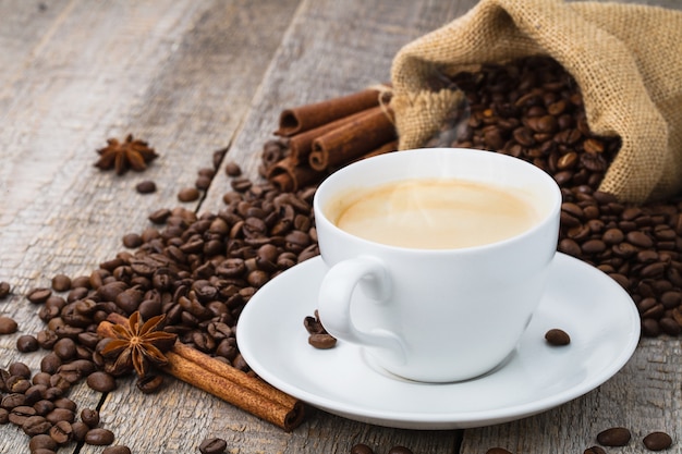 Kaffeetasse auf altem Holztisch und Beutel mit Kaffeebohnen