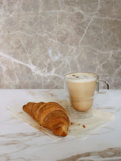 Kaffeetasse aus Glas mit Croissant im Hintergrund