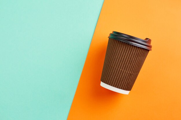 Kaffeetasse aus Papier auf orange und türkisfarbener Oberfläche