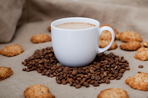 Kaffeetasse mit Bohnen und Keksen Cappuccino weißer Becher Kaffeebohnen Süßigkeiten auf dem Hintergrund