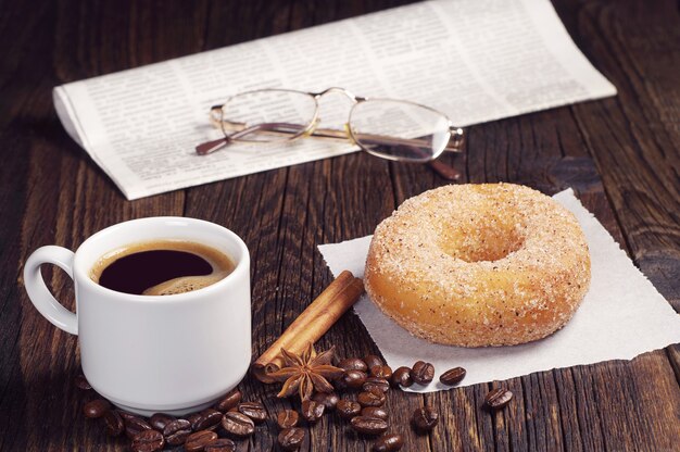 Kaffeetasse mit Donut und Zeitung auf dunklem Holztisch