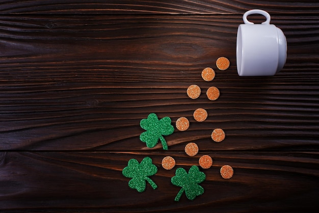 Kaffeetasse mit dreiblättrigen Shamrock handgemachten Blättern und Münzen auf Holzhintergrund