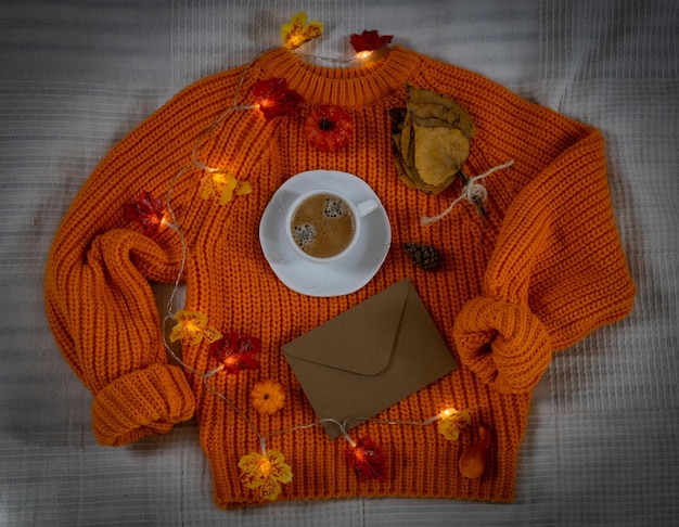 Kaffeetasse mit Girlande verlässt Kürbis und Tannenzapfen auf einem orangefarbenen Pullover