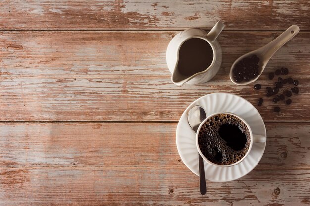 Kaffeetasse mit Kaffeebohnen und Milchkännchen auf Vintage-Holzoberfläche Kopierbereich Selektiver Fokus