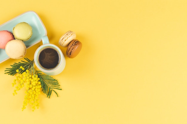 Kaffeetasse mit Macarons und gelber Blumendekoration auf Gelb. Draufsicht.