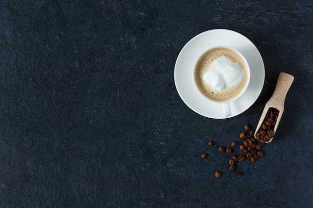 Kaffeetasse mit Milch und gerösteten Kaffeebohnen auf Draufsicht des schwarzen Hintergrundes