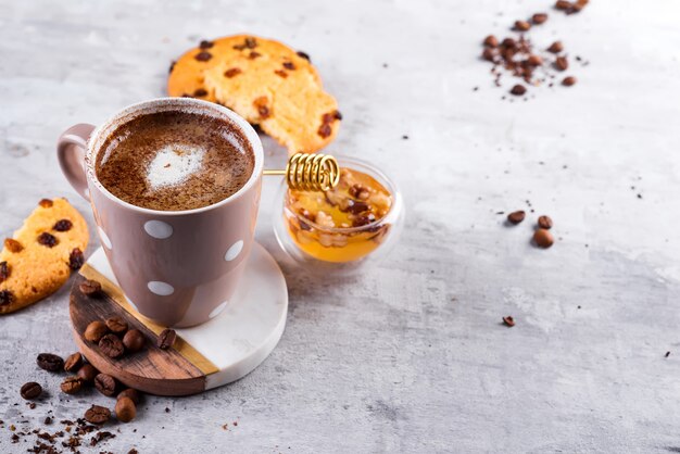 Kaffeetasse mit Schokoladenplätzchen auf Steinhintergrund mit Honig- und Metallhonigstock