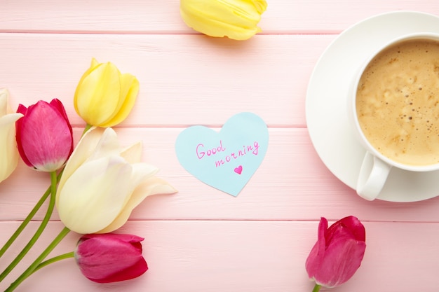 Kaffeetasse mit Tulpenblüten und Notizen Guten Morgen auf rosa Oberfläche, Frühstück am Muttertag oder Frauentag