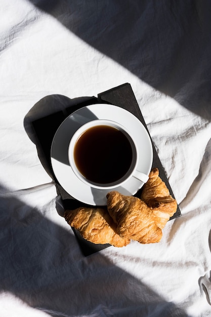 Kaffeetasse und Croissants auf dem Bett im Morgensonnenlicht