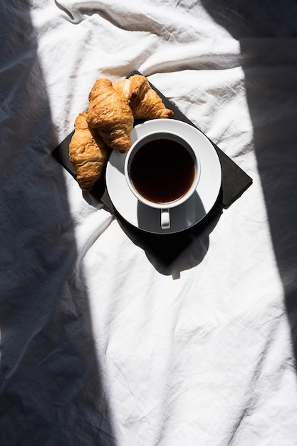 Kaffeetasse und Croissants auf dem Bett im Morgensonnenlicht