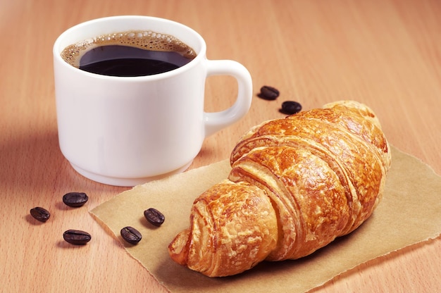 Kaffeetasse und frisches Croissant auf dem Schreibtisch